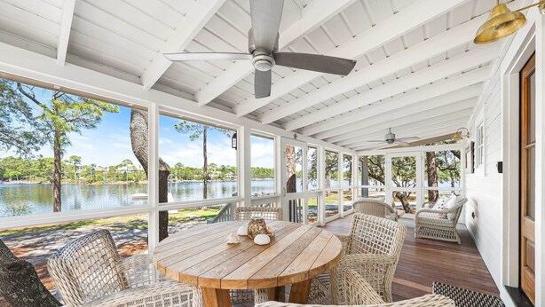 A covered outdoor area with a round wooden table and wicker chairs, overlooking a body of water.
