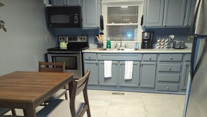 A kitchen with a wooden table and chairs, a microwave, stove, sink, and cabinets.
