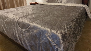 A neatly made bed with a grey patterned bedspread, a bedside lamp, and a wooden headboard.