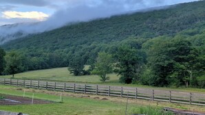 A rural landscape with a wooden fence, green fields, and a forested hill.