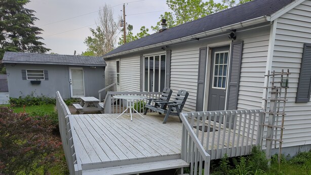 A house with a porch, a table, and chairs. There is a small garden area with bushes and a tree.