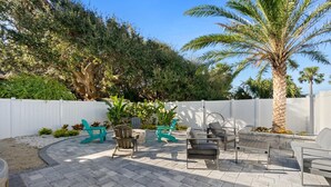 An outdoor patio with a stone-tiled floor, a white fence, and a variety of seating including chairs and a bench.