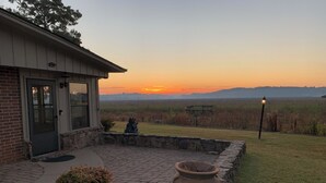 Et hus med murstensfacade, stenbelagt terrasse og udsigt til solnedgang over et mark.