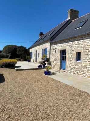 Charming stone building with a sloped roof, featuring windows with shutters and a chimney.