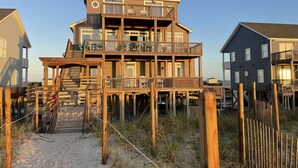 A multi-story wooden house with a balcony on the second floor, situated on a sandy beach with wooden fencing. - beach front home pool  many new upgrades (North Topsail Beach)