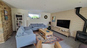 Een woonkamer met een bank, salontafel, televisie, open haard, boekenkast en een stenen muur.