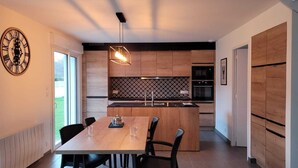 Een moderne keuken met houten kasten, een centraal eiland en een eethoek met een houten tafel en stoelen.