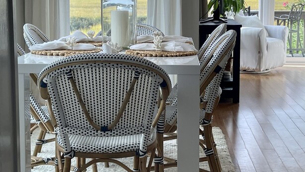 A dining area with wicker chairs, a white table, and a view of a field through large windows. - Tennis Courts in front, and the ever changing Marsh in back. Golf cart included. (Fripp Island)