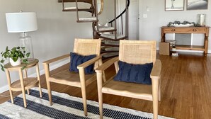 A modern living room with a wooden staircase, two wooden chairs with cushions, a small side table, a lamp, and a console table with decorative items. - Tennis Courts in front, and the ever changing Marsh in back. Golf cart included. (Fripp Island)