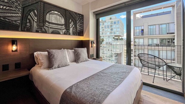 A modern hotel room with a large bed, a balcony with a view of the city, and a decorative wall panel. - Luxury stay in Condesa | Rooftop, Pool & Views (Ciudad de México)