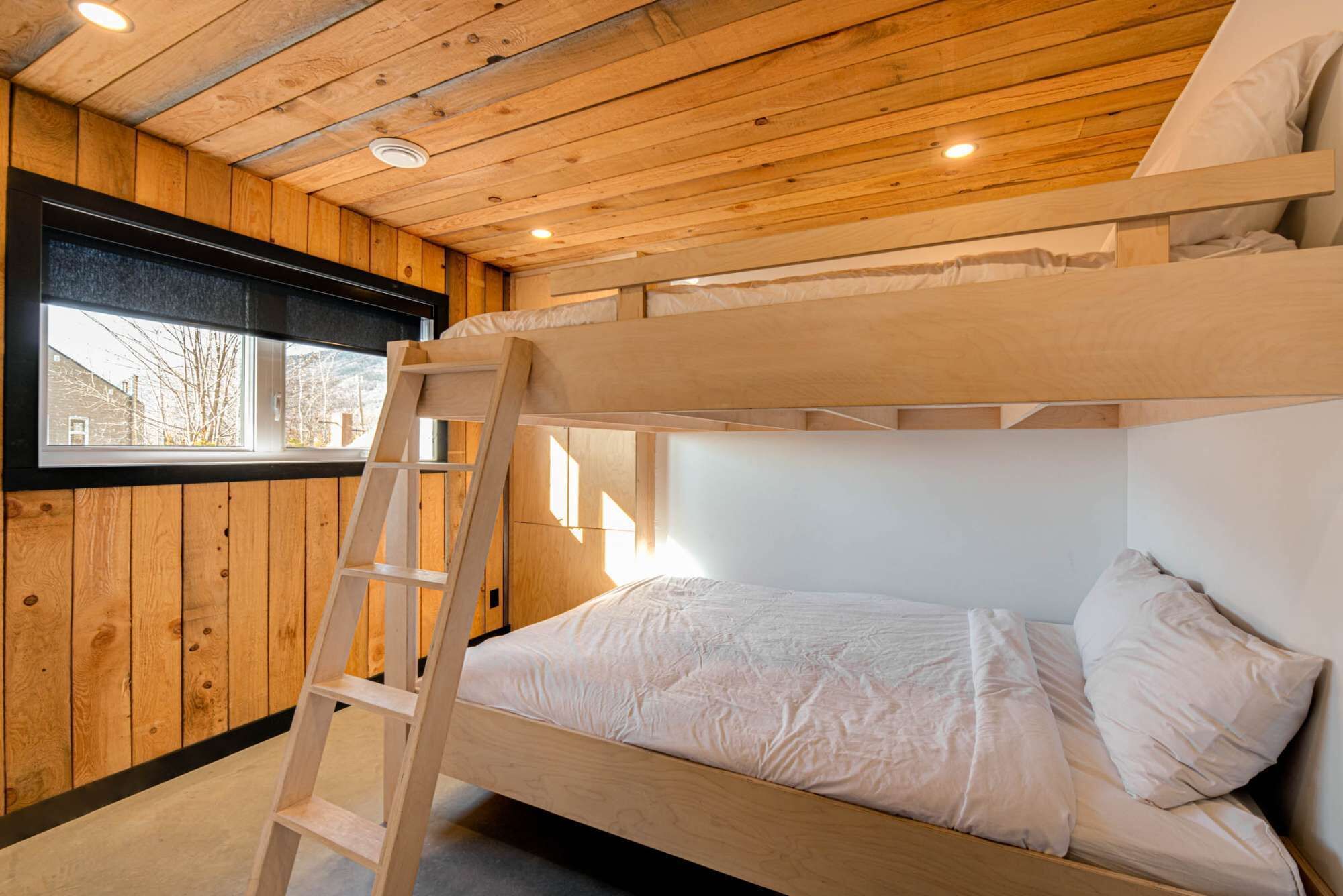 A bunk bed room with wooden walls, a window, and a ladder.