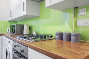 A modern kitchen with a gas stove, microwave, and stainless steel appliances. There are three gray containers labeled sugar, tea, and coffee. - Inviting 2-bed House in Milton Keynes - Netflix (Milton Keynes)