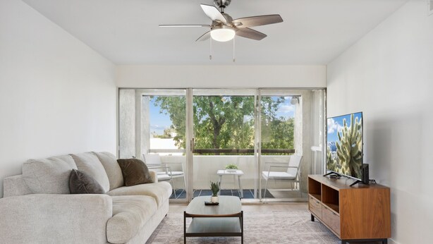 A living room with a sofa, coffee table, TV stand, and a view through large sliding glass doors to an outdoor patio. - Condo in Scottsdale (Scottsdale)