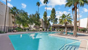 A swimming pool with clear blue water, surrounded by palm trees and lounge chairs. - Condo in Scottsdale (Scottsdale)