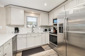 Una cocina moderna con armarios blancos, un refrigerador de acero inoxidable y un microondas.