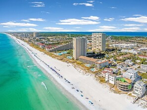 An aerial view of a coastal area with a beach, buildings, and a clear sky.