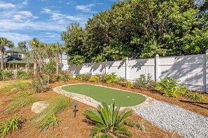 A landscaped garden with a putting green, a white fence, and various plants.