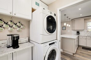 A modern kitchen with a built-in washer and dryer, a coffee maker, and a hanging rack for mugs.