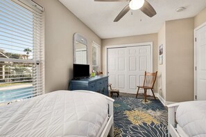 A bedroom with two beds, a dresser, a television, a ceiling fan, and a view of a pool.