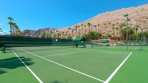 Un court de tennis avec un filet, entouré de palmiers et avec une montagne en arrière-plan.