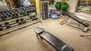 Une salle de sport équipée d’un banc, d’haltères et de ballons d’exercice.