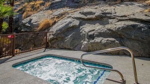 Un bain à remous doté d’une balustrade en métal, entouré d’une colline rocheuse et de palmiers.