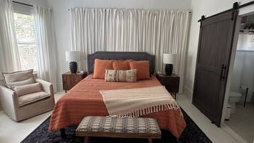 A bedroom with a bed, a bench, a chair, a nightstand, a lamp, a ceiling fan, and a sliding door.