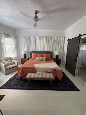 A bedroom with a bed, a bench, a chair, a nightstand, a lamp, a ceiling fan, and a sliding door.