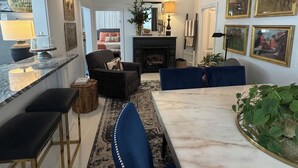 Een moderne woonkamer met een open haard, een eethoek met een marmeren tafel en een bar met krukken.