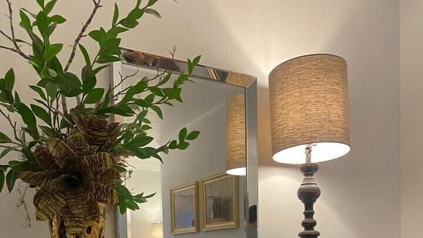 Een open haard met een spiegel erboven, een lamp aan de rechterkant en een plant in een vaas op de schoorsteenmantel.