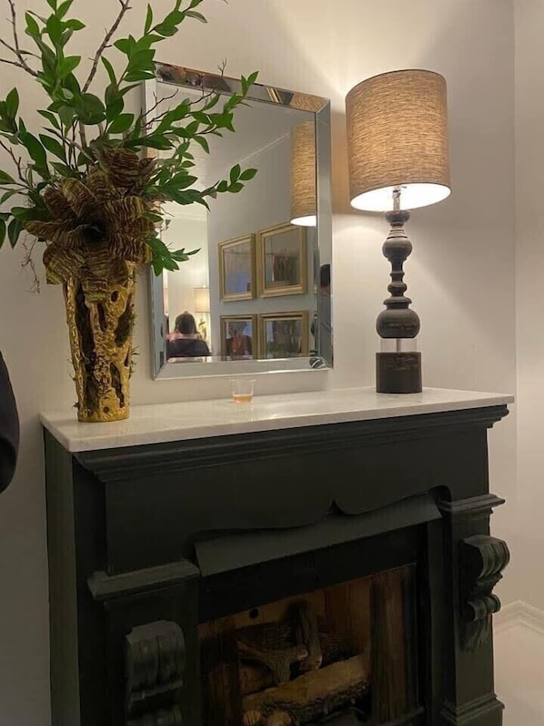 A fireplace with a mirror above it, a lamp to the right, and a plant in a vase on the mantel.
