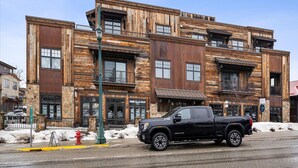 Un immeuble à plusieurs étages, doté d’une façade en bois rustique, de grandes fenêtres et d’un camionnette noire garée devant.