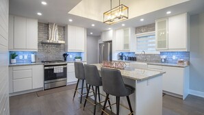 Una cocina moderna con armarios blancos, una isla central con taburetes y una campana extractora de acero inoxidable.