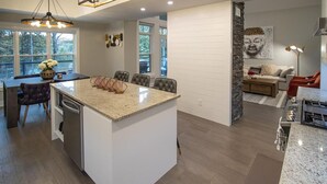 Una cocina moderna con una isla central, un comedor con mesa y sillas, y una sala de estar con sofá y mesa de centro.