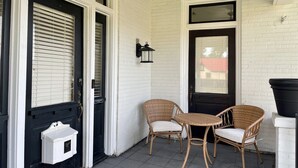 A covered porch with white brick walls, two wicker chairs, a small white mailbox, and a black door. - Gem on Spring-Upscale home walk to Main sleeps 11 (Del Rio)