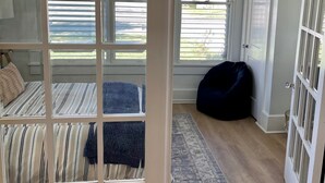 A room with a bed, a dark bean bag chair, a patterned rug, and a view through a window with blinds. - Gem on Spring-Upscale home walk to Main sleeps 11 (Del Rio)