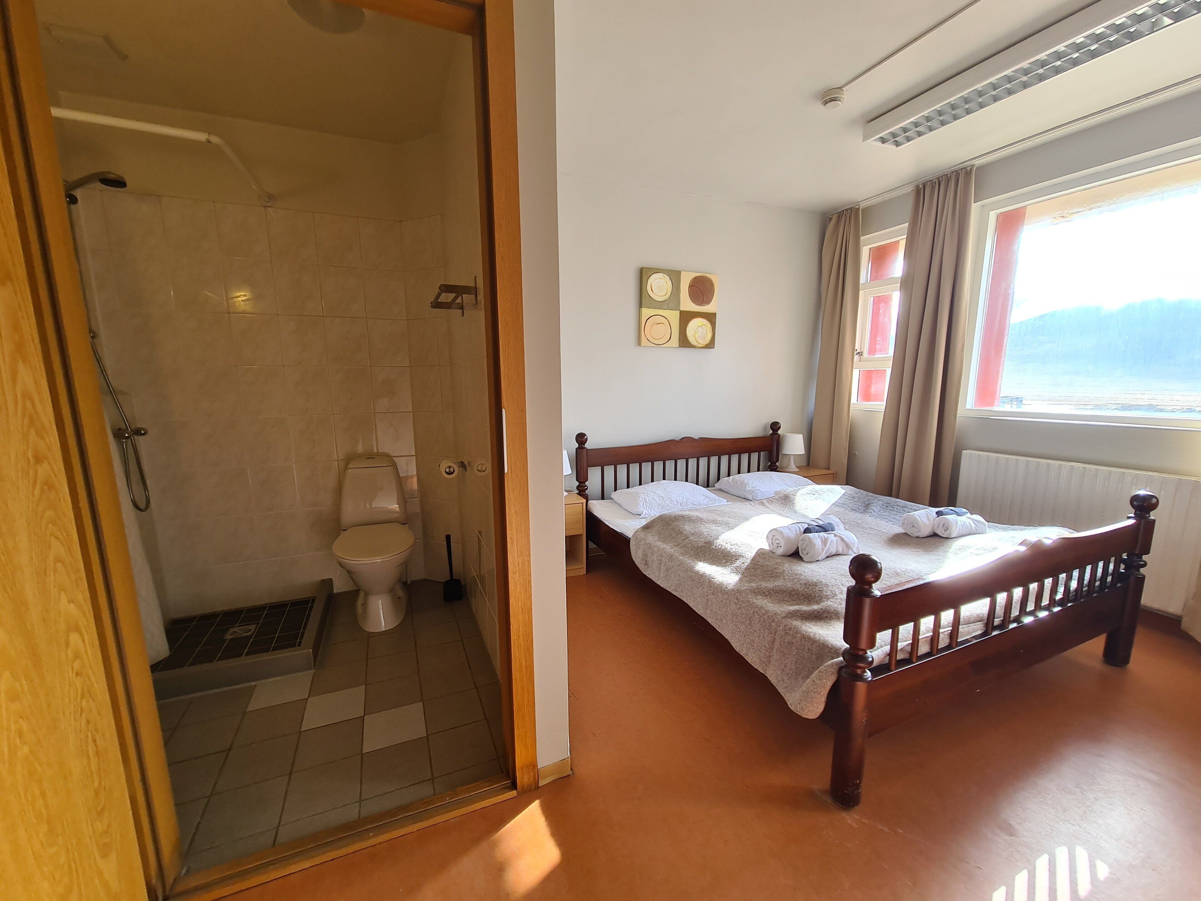 A hotel room with a wooden bed, a bathroom with a shower, and a window with a view.