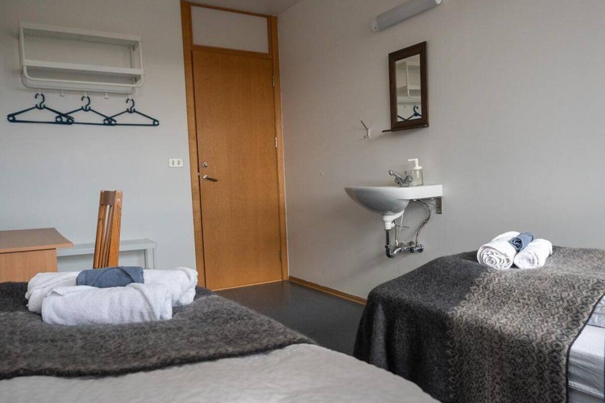 Habitación de hotel con dos camas, una puerta de madera, un lavabo blanco, un espejo y un perchero.