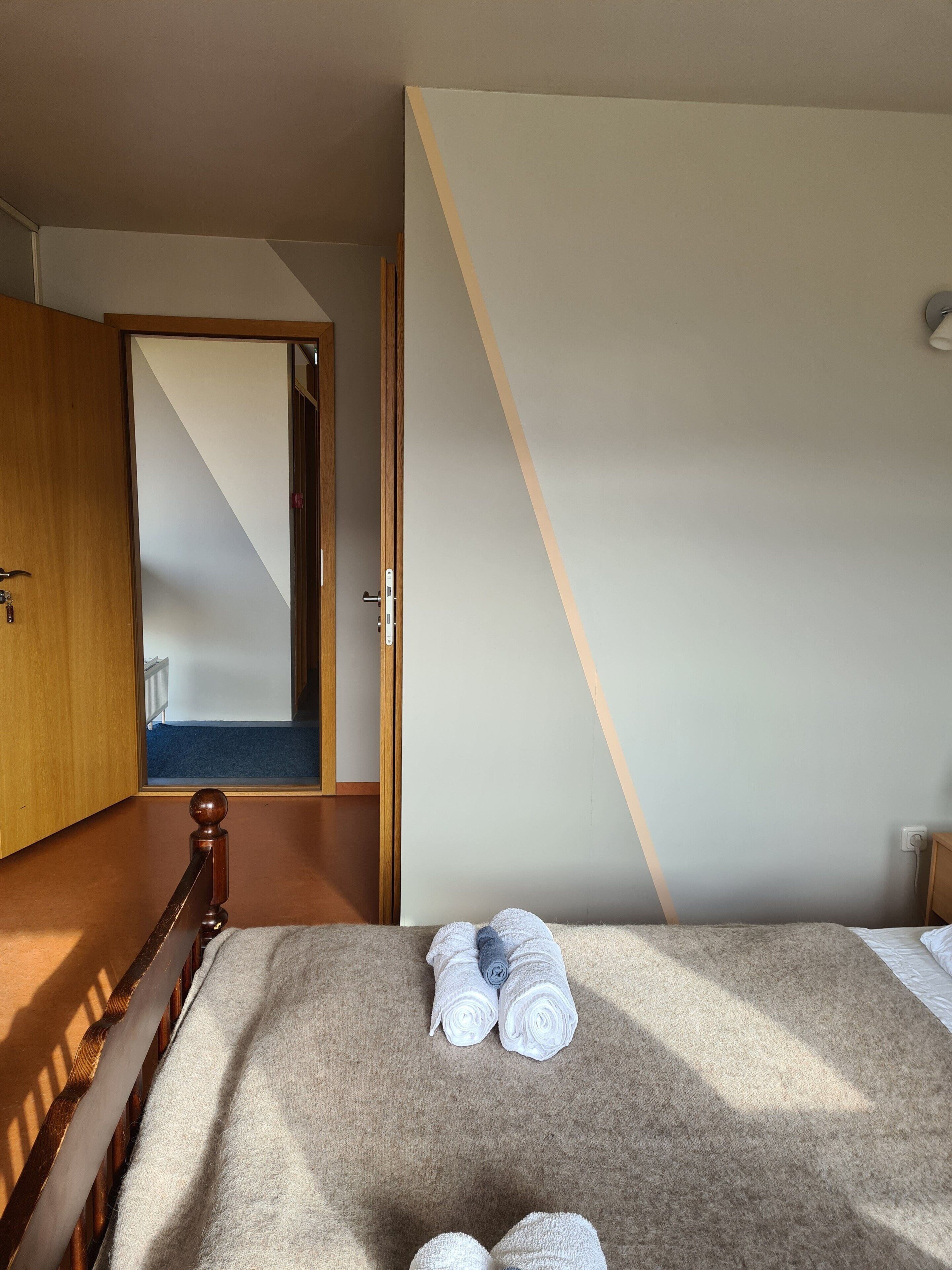 A bedroom with a bed, a wooden headboard, a carpeted floor, and a door leading to another room.
