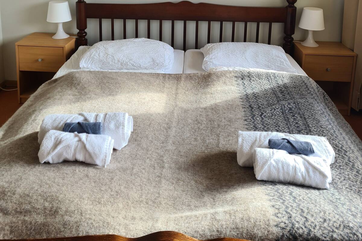 Una cama bien tendida con un edredón estampado, dos mesitas de noche con lámparas y una obra de arte en la pared sobre la cama.