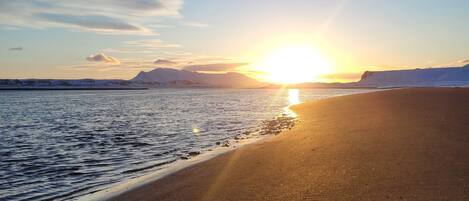 A beach with a sunset over the water, a clear sky, and distant mountains.
