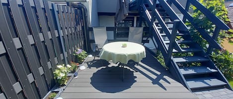Een terras met een ronde tafel en stoelen, een houten hek en een trap.