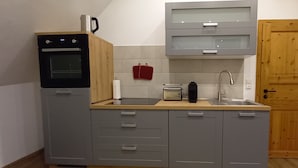 Cocina compacta con armarios grises, horno empotrado, pileta y puerta de madera.