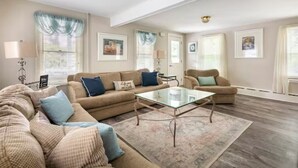 Una sala de estar con un sofá color beige, una mesa de centro de cristal y una alfombra estampada.