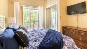 Un dormitorio con cama, cómoda, televisor y balcón con cortinas.