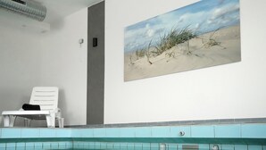 Een zwembadgedeelte met een witte ligstoel, een schilderij van een strand en een betegelde muur.