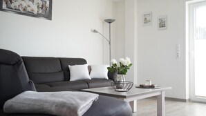 Een moderne woonkamer met een donkergrijze bank, witte kussens, een salontafel met een vaas witte bloemen en een vloerlamp.
