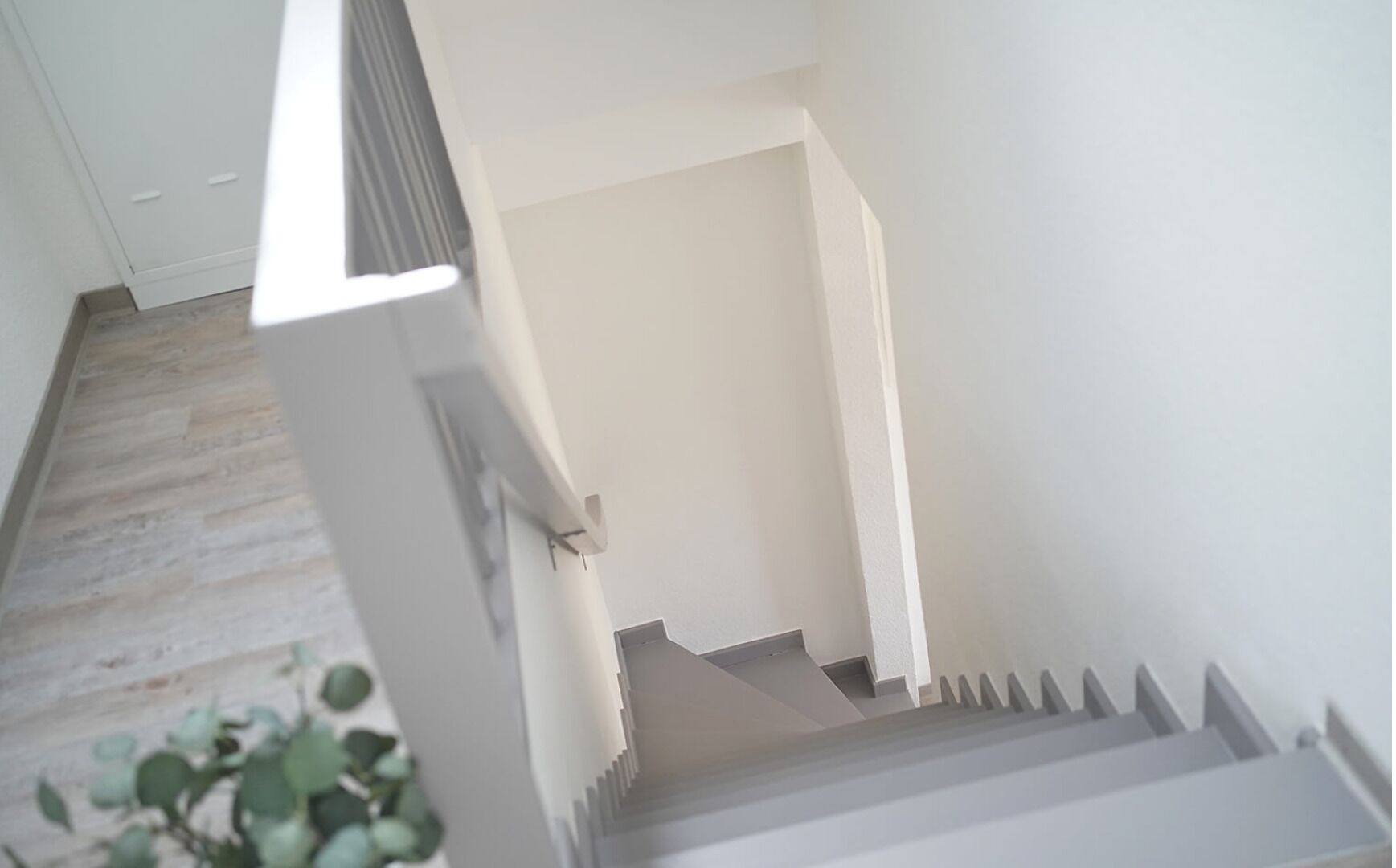 A staircase with a handrail, leading to a landing with a white wall and a door.