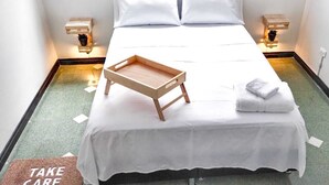 A neatly made bed with a wooden tray and folded towels, two bedside lamps, and a "TAKE CARE" mat.