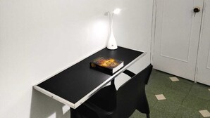 A small room with a desk, a chair, a white door, and a colorful painting on the wall.
